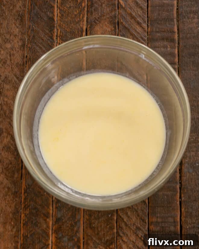 Buttermilk is carefully poured into the bowl containing the whisked egg, salt, and sugar mixture, ready to be combined.