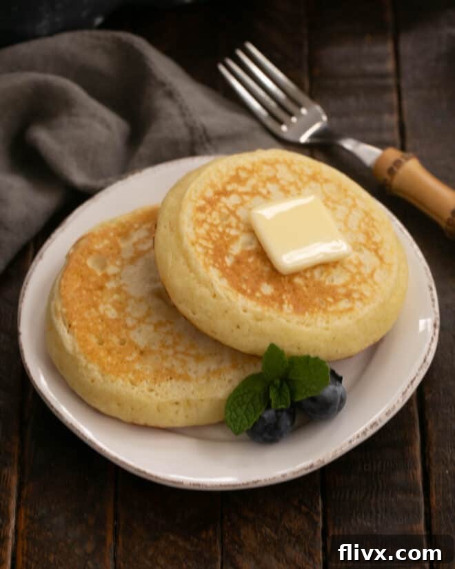 Two buttermilk pancakes on a white plate with a pat of butter.