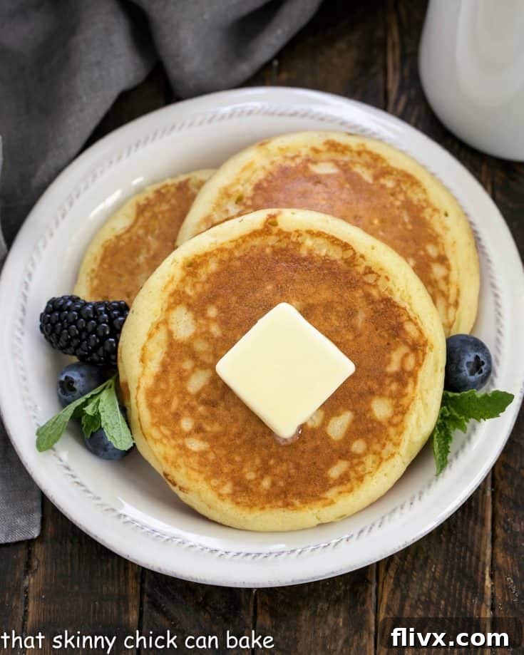Overhead view of 3 buttermilk pancakes topped with butter and garnished with berries and mint