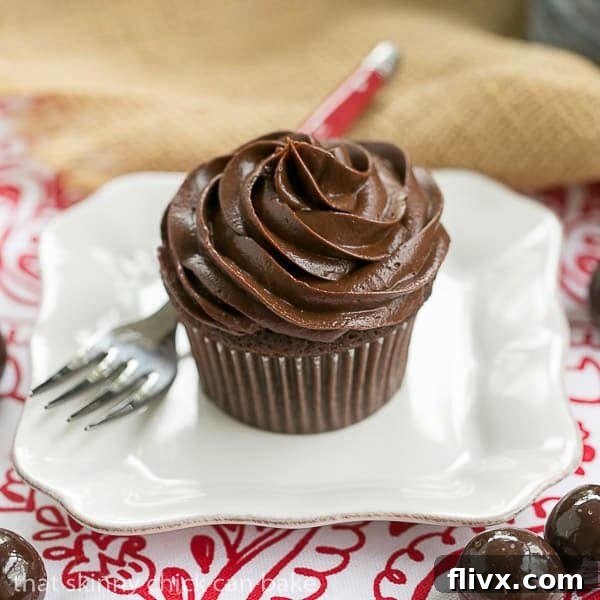 A single chocolate cupcake with a swirl of decadent chocolate buttercream on white plate with a fork.