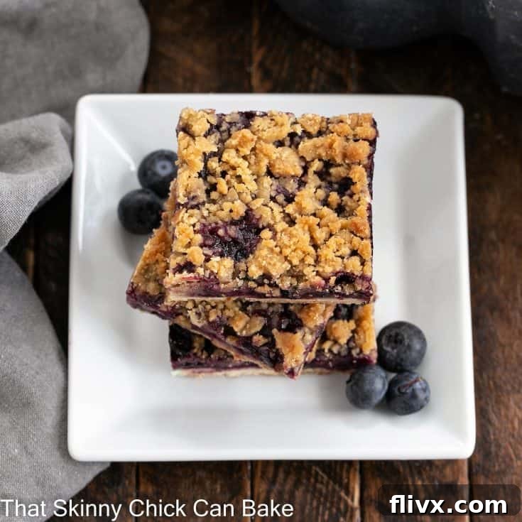 stack of blueberry streusel bars on a white ceramic plate, garnished with fresh blueberries