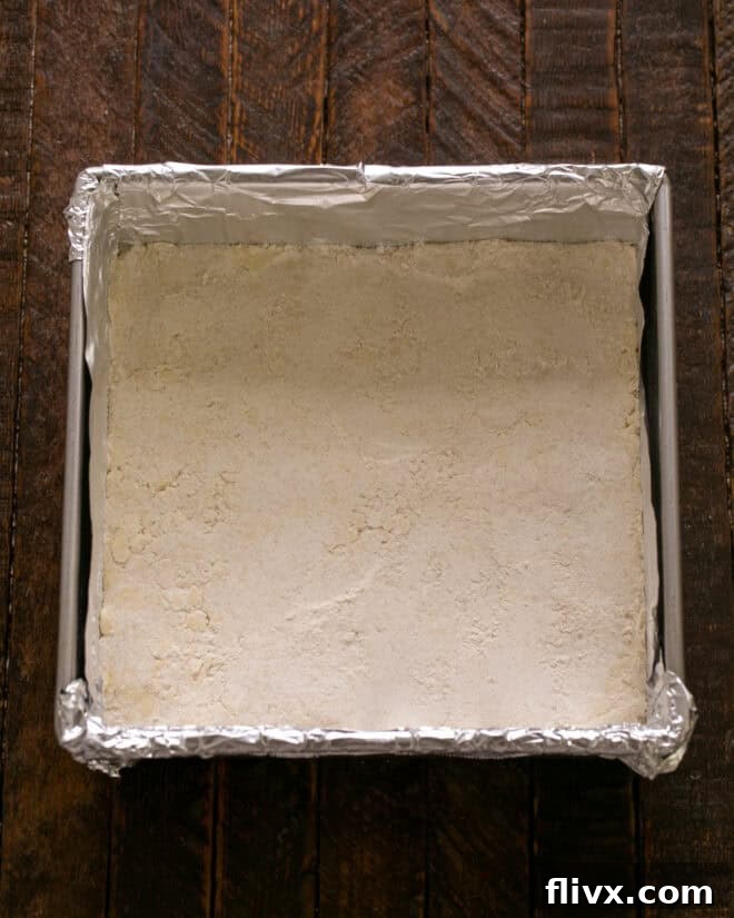 Pressing the buttery crust mixture evenly into a prepared baking pan.