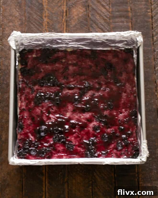 Spreading a layer of melted blueberry jam over the warm, pre-baked shortbread crust.