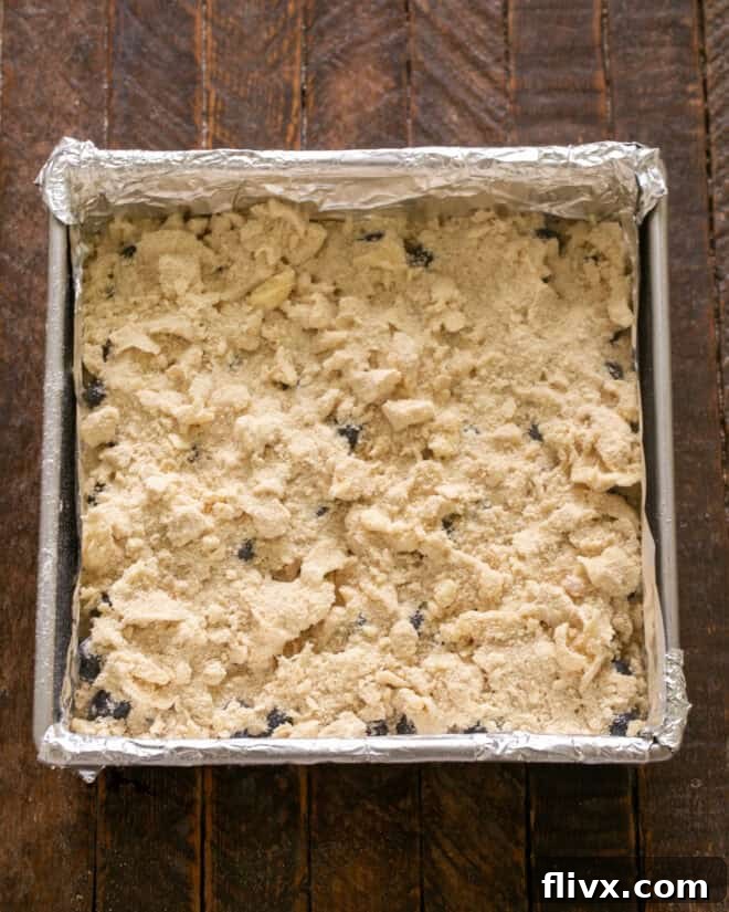 Crumbly streusel topping being sprinkled generously over the blueberry layer.