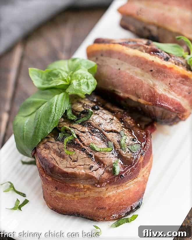 Grilled Beef Tenderloin Steaks wrapped in crispy bacon and generously topped with melted garlic herb butter, presented on a pristine white platter.