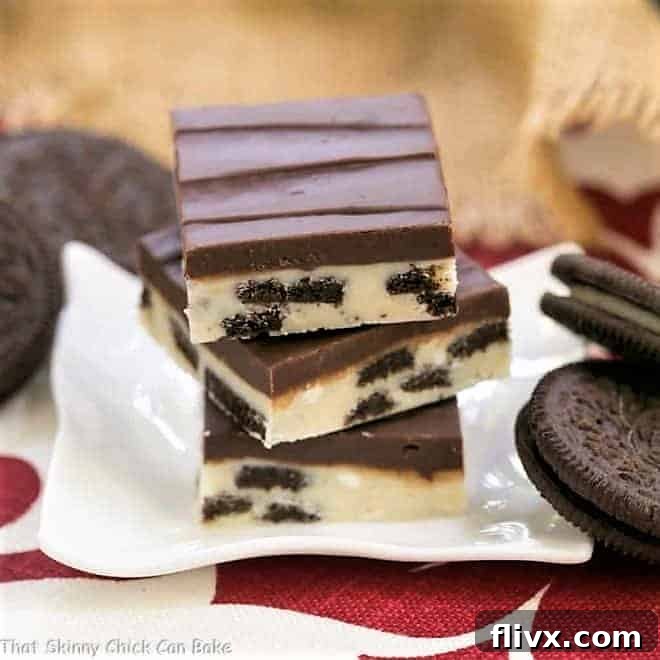A stack of luxurious Double Decker Oreo Fudge squares on a pristine white ceramic plate, showcasing distinct layers of white and dark chocolate with visible Oreo chunks.