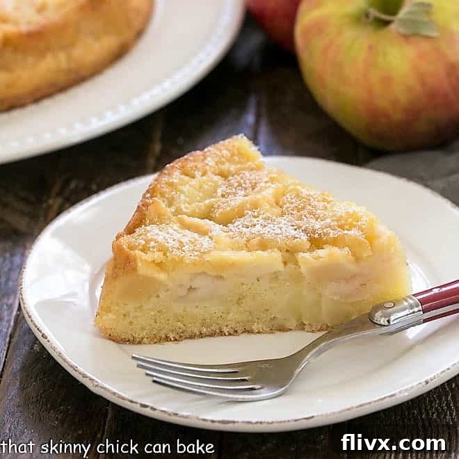 A slice of French apple cake on a round white plate, showcasing the dense apple filling and golden crust.