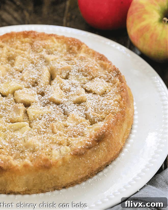 An uncut French Apple Cake on a white cake plate, golden brown and inviting.