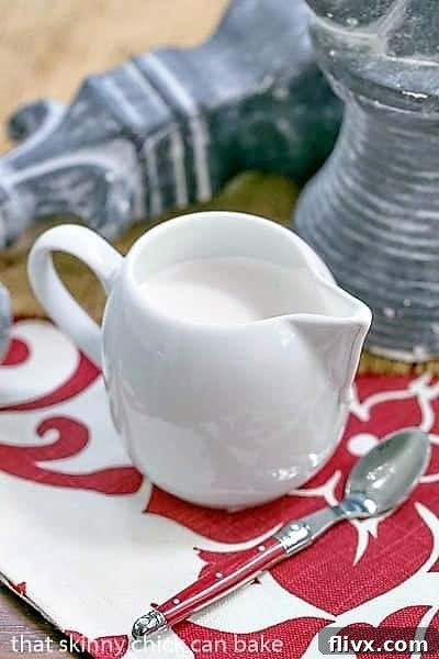 A pristine white ceramic pitcher overflows with glistening, homemade marshmallow cream sauce, ready to be drizzled over a delicious dessert. The smooth, inviting texture of the sauce is beautifully highlighted against the pitcher, suggesting a sweet and versatile topping.