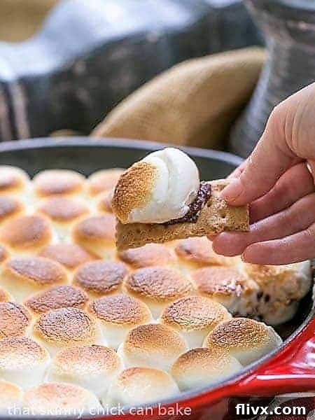 A close-up view of Skillet S'mores Dip, with a single graham cracker scooping up a generous bite of melted chocolate ganache and gooey toasted marshmallow.
