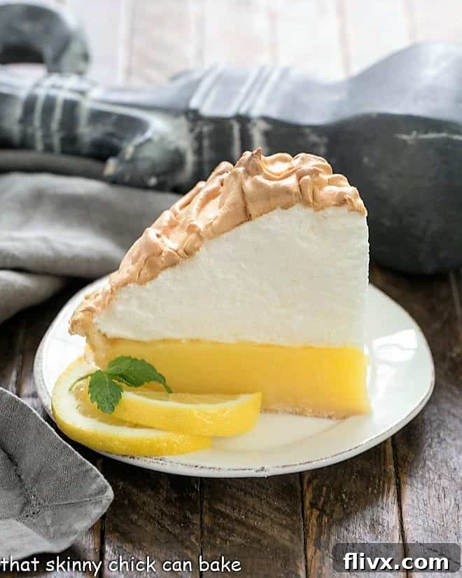 A perfectly sliced piece of Mile High Lemon Meringue Pie on a pristine white plate, showcasing its layers.