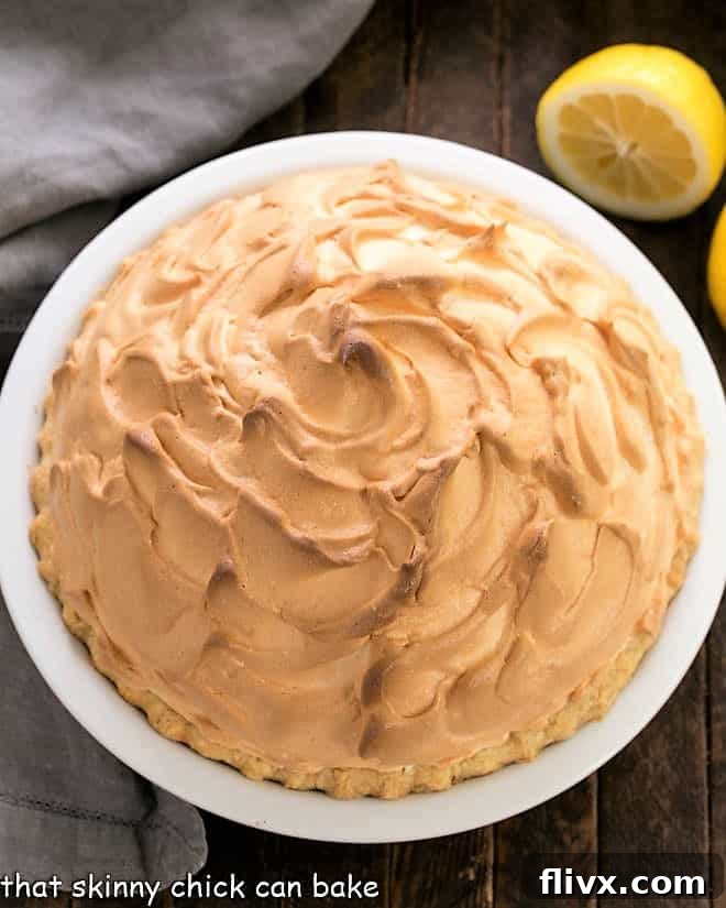 Overhead shot of a golden-brown lemon meringue pie in a elegant white ceramic pie dish, showcasing its fluffy topping.
