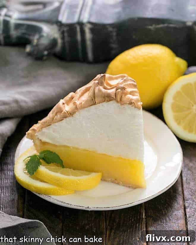 A delectable slice of Mile High Lemon Meringue Pie, beautifully garnished with fresh lemon slices and a sprig of mint, on a white dessert plate.