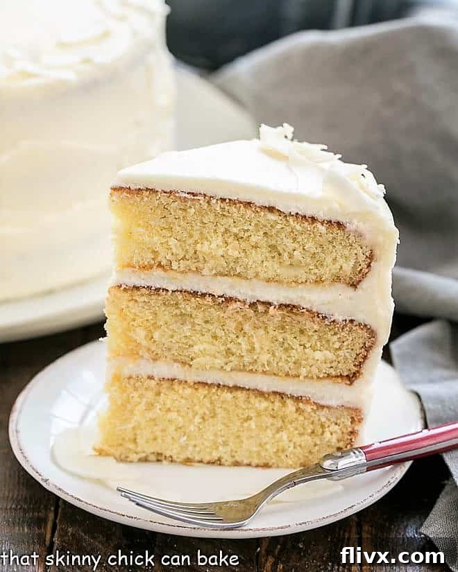 A perfectly sliced piece of Italian Cream Cake, revealing three moist coconut cake layers and generous cream cheese frosting, resting on a pristine white dessert plate.