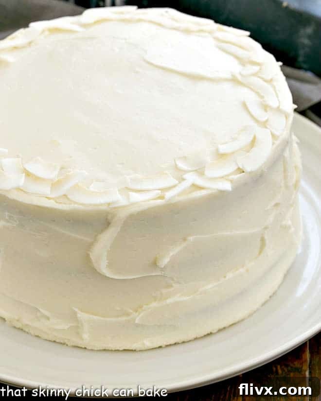 A side view of the Italian Cream Cake, showcasing its impressive height and three distinct layers, generously covered in fluffy cream cheese frosting, presented on an elegant white serving plate.