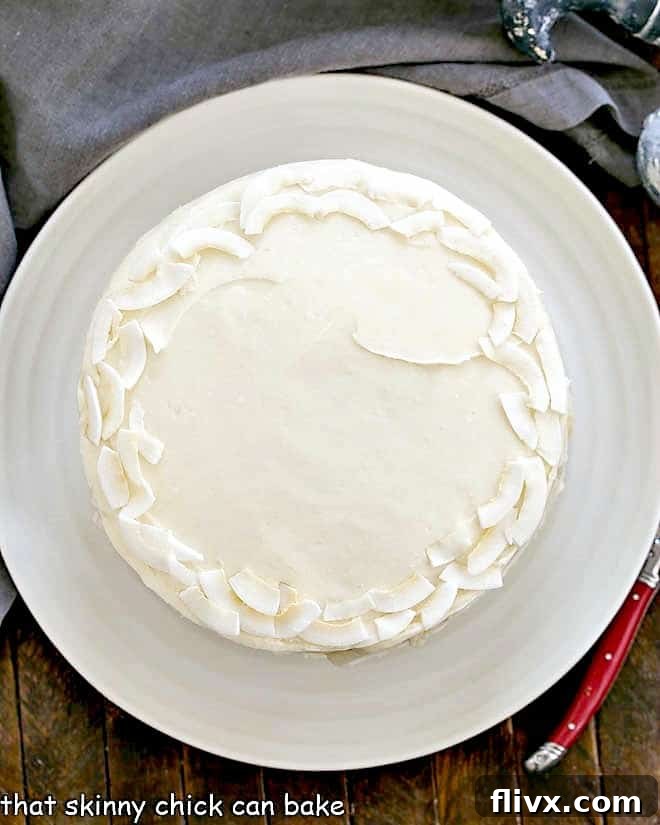 An overhead shot capturing the full glory of a frosted Italian Cream Cake, adorned with coconut flakes, presented on a pristine white cake plate.