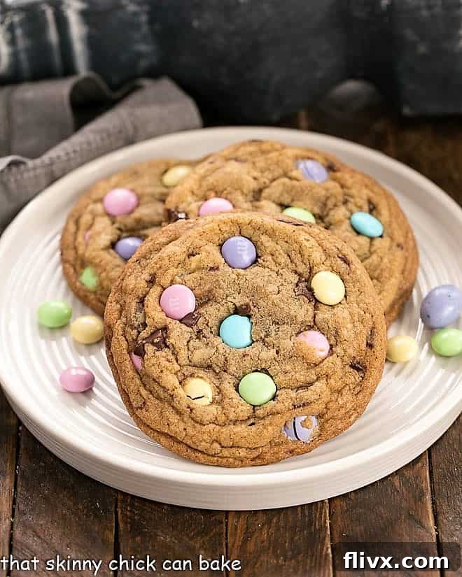 Three perfectly baked Brown Butter Easter Cookies adorned with pastel M&M's, artfully arranged on a pristine white plate, surrounded by scattered candies.