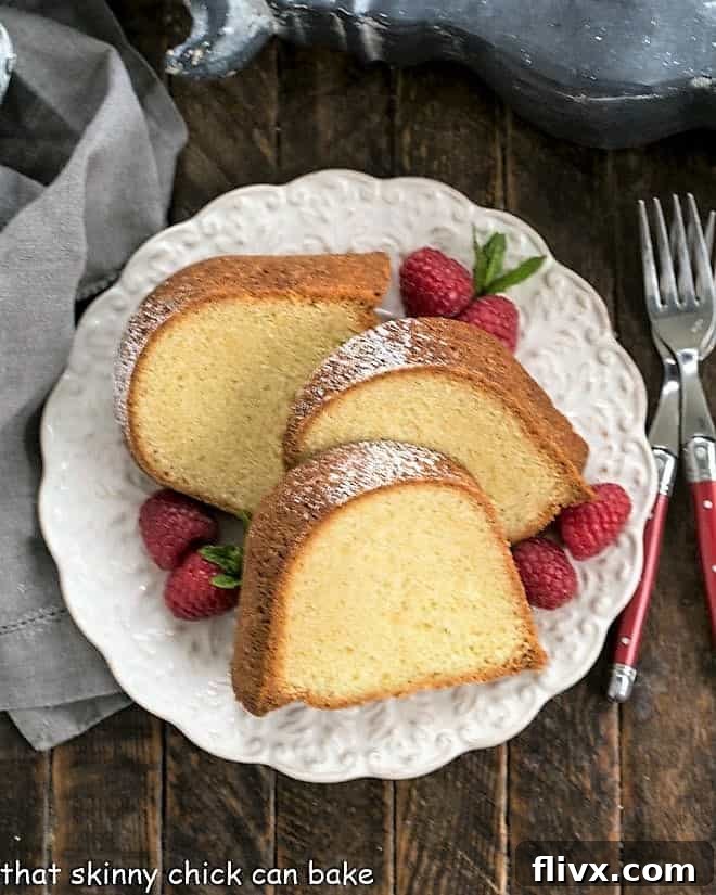 Overhead view of a beautifully baked Sour Cream Pound Cake on a white serving plate, garnished with fresh raspberries and a sprig of mint, ready for slicing.
