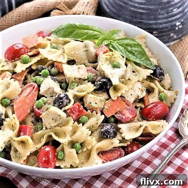 A beautifully presented Pesto Pasta Salad in a shallow white serving bowl with a silver serving spoon, ready to be enjoyed.