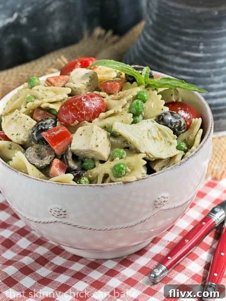 A close-up view of the vibrant Pesto Pasta Salad served in a white bowl, garnished with two red-handled forks.