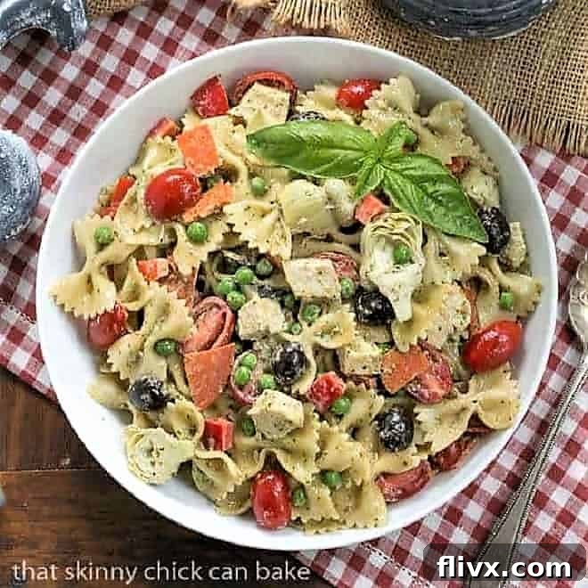 An inviting overhead view of a hearty Pesto Pasta Salad, served in a white bowl, resting on a charming red and white checkered napkin.