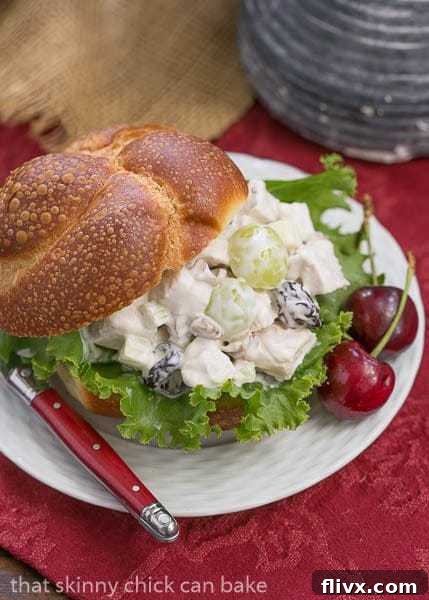 A beautifully composed plate featuring a gourmet Chicken Salad sandwich on a perfectly toasted bun, garnished with two fresh cherries and accompanied by a fork, inviting a delightful culinary experience.