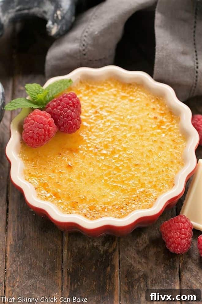 A vibrant red ramekin holds a beautifully prepared White Chocolate Crème Brûlée, showcasing its rich, creamy texture and golden, caramelized sugar topping, inviting a spoonful.