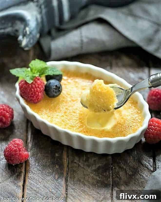 A close-up of a White Chocolate Crème Brûlée in a white ramekin, with a spoon having just cracked through the crisp sugar topping, revealing the creamy custard beneath.