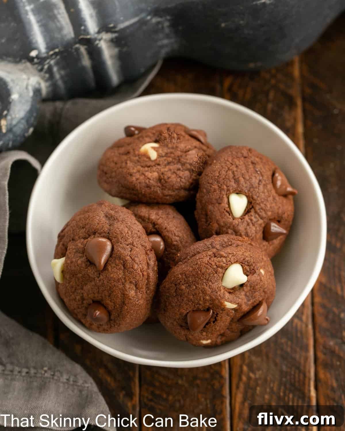 Ultimate Triple Chocolate Chip Cookies 2 A pristine white bowl filled with five perfectly baked Triple Chocolate Chip Cookies, showcasing their rich, dark hue and a generous scattering of varied chocolate chips. A close-up view inviting a delicious bite.