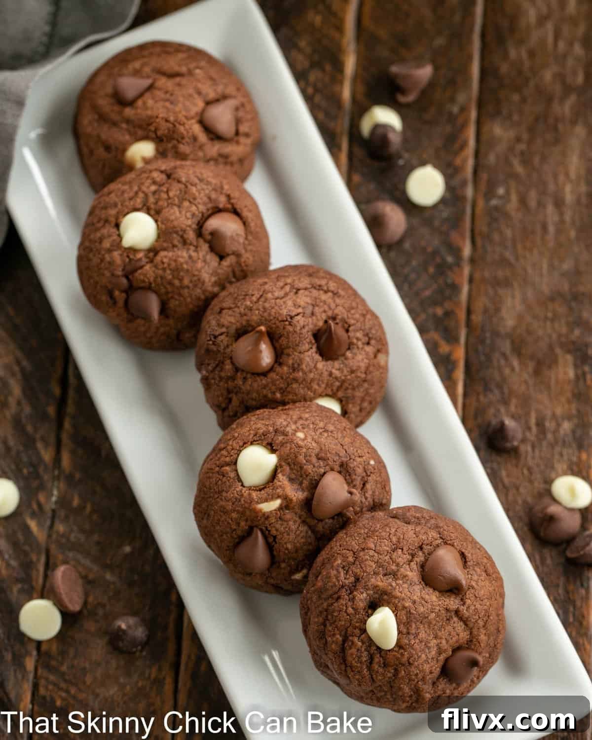 Ultimate Triple Chocolate Chip Cookies 3 An overhead shot showcasing a selection of dark, rich chocolate chocolate cookies meticulously arranged on a narrow, elegant white ceramic tray, highlighting their perfect texture and enticing appearance.
