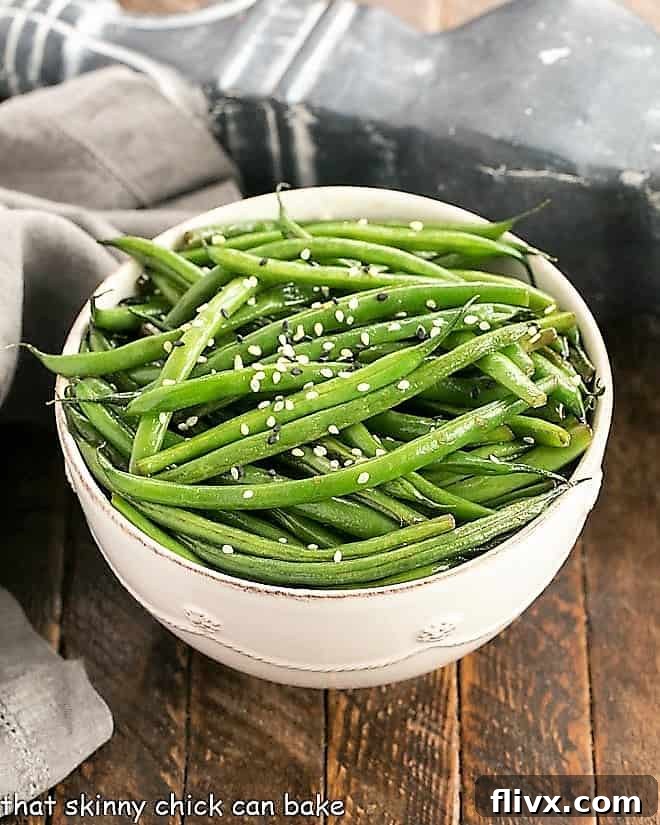 An overhead shot of glossy, perfectly sautéed Asian Green Beans nestled in a white ceramic bowl, ready to be served.