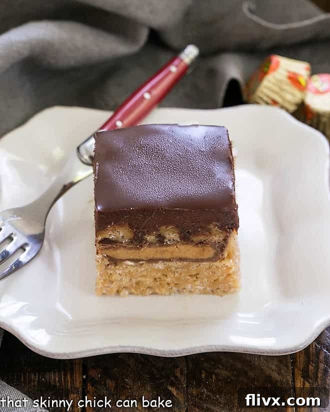 A Stuffed Peanut Butter Rice Krispie Treat with a chocolate ganache topping sits on a square white plate, accompanied by a red-handled fork, inviting a delicious taste.