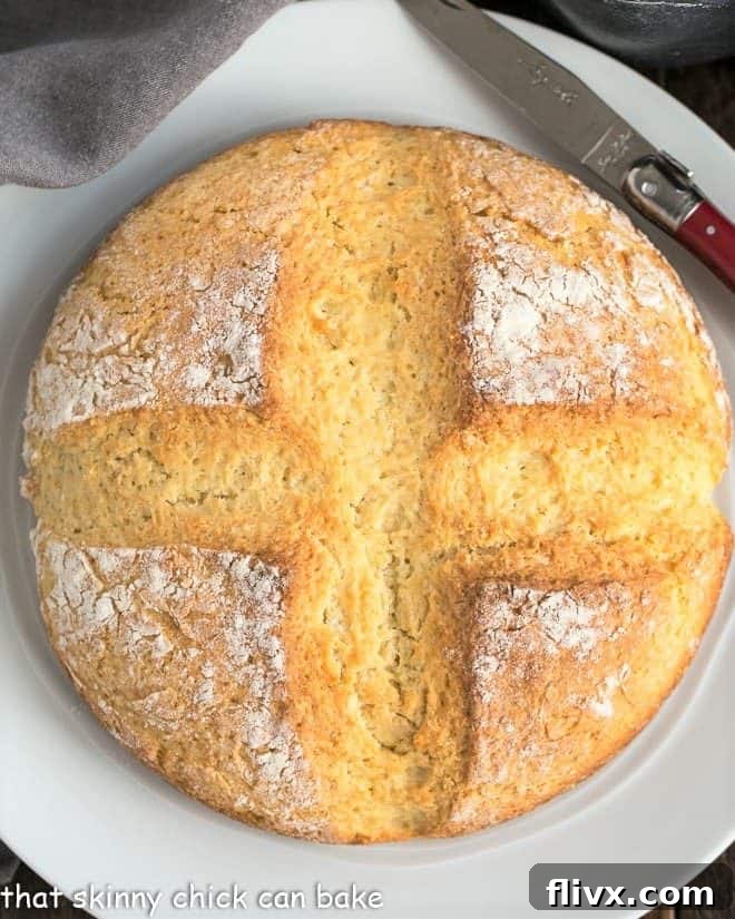 Irish Soda Bread - a simple quick bread that's slightly sweet, tender and delicious! Freshly baked Irish Soda Bread on a pristine white plate, showcasing its rustic crust and inviting texture.