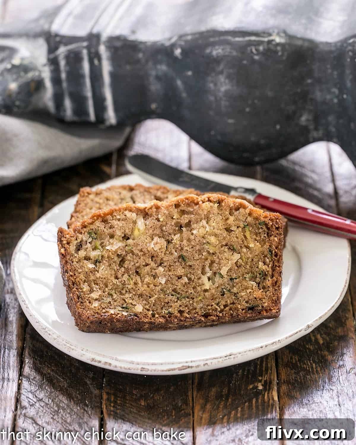 Slices of golden-brown zucchini bread recipe with visible pineapple and coconut pieces, served on a white plate alongside a red-handled knife.
