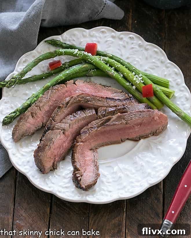 Easy Grilled Flank Steak slices on a white dinner plate with asparagus, perfectly cooked and ready to serve.