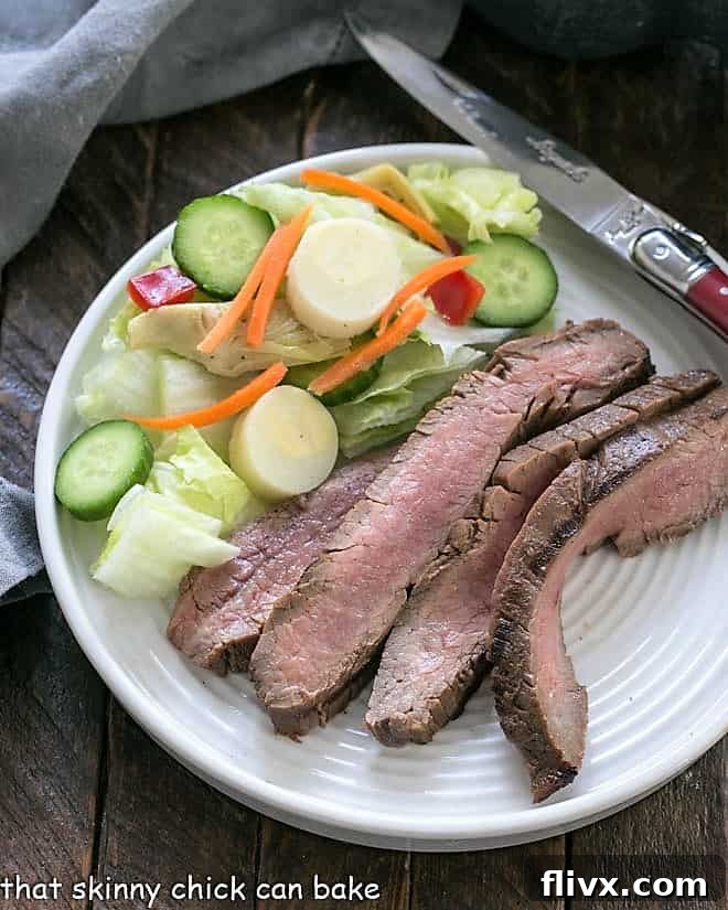 Overhead view of Easy Grilled Flank Steak on a dinner plate with a vibrant green salad, showcasing perfectly sliced meat.