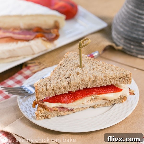A perfectly sliced half of a Roasted Chicken, Brie, and Bacon Sandwich artfully placed on a white luncheon plate.