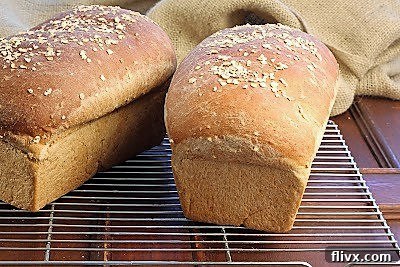Two golden-brown loaves of freshly baked honey oatmeal bread cooling on a wire rack, promising a delightful texture and sweet aroma.
