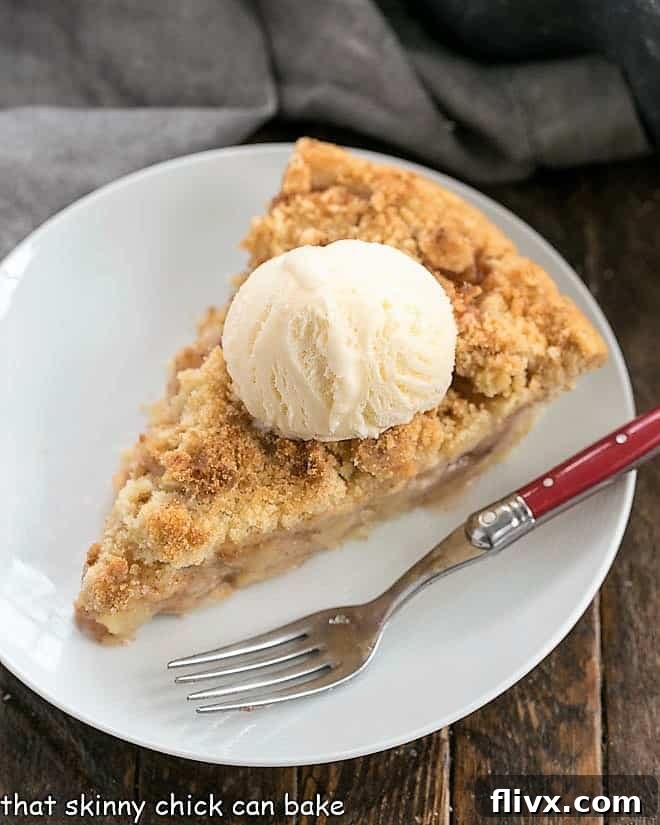 A pristine slice of Dutch Apple Pie rests on a white plate, accompanied by a red-handled fork, inviting indulgence in its crumbly top and tender filling.