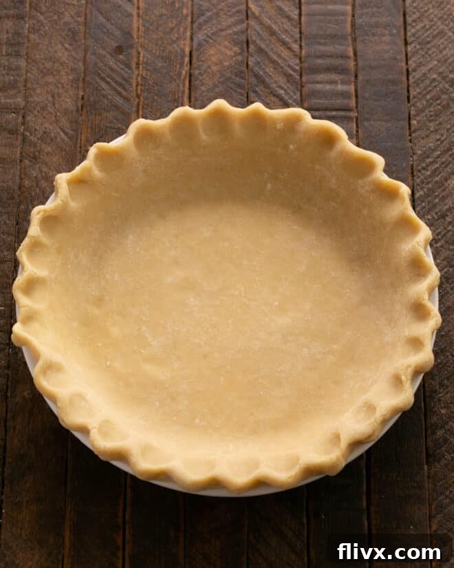 The first step in making Dutch Apple Pie: fitting pre-made or homemade pie dough into a pie plate and carefully fluting the edges for a decorative finish.