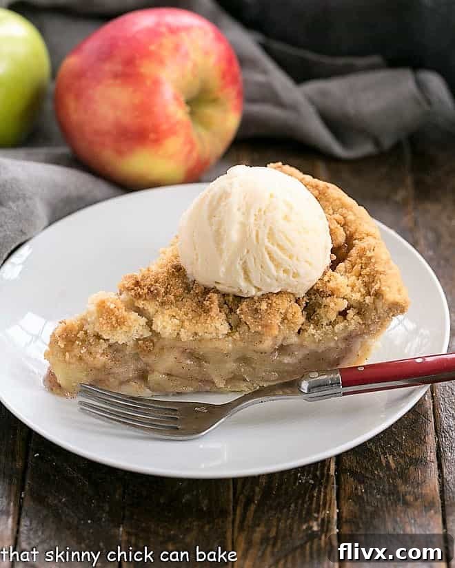 A beautiful slice of the best apple pie recipe, served on a white plate and garnished with a scoop of melting vanilla ice cream, ready to be enjoyed.