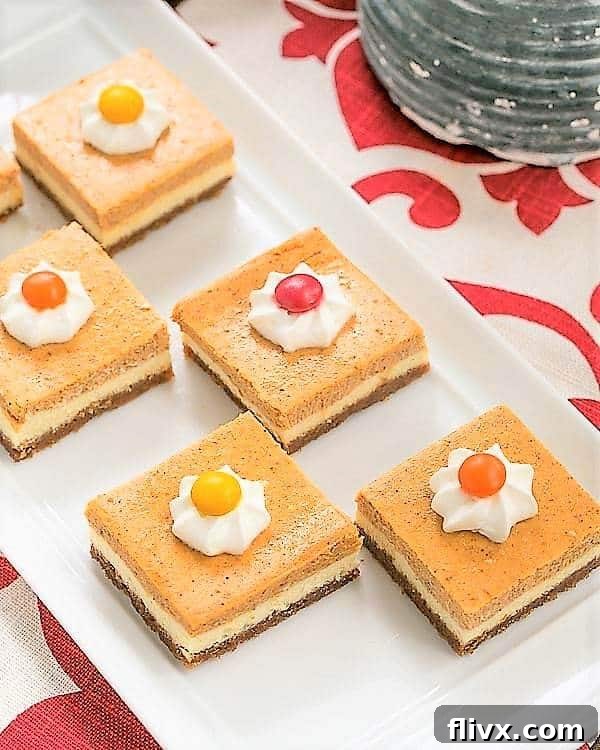 Two pieces of Pumpkin Cheesecake Bars displayed on a white ceramic tray, showcasing their beautiful layers.