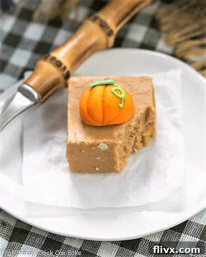 A piece of Easy Pumpkin Fudge on a white plate with a bite taken out, decorated with a small candy pumpkin for a festive touch.