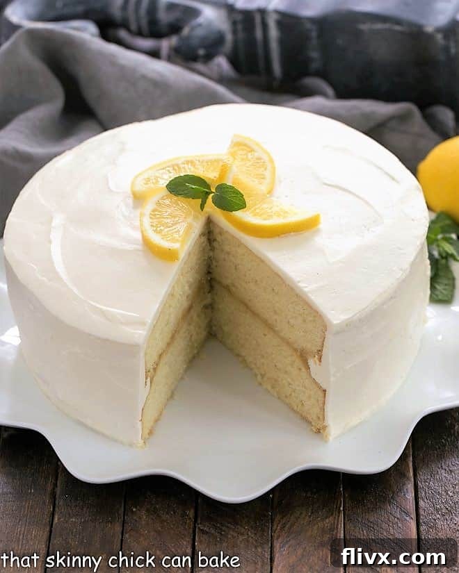 A stunning four-layer Lemon Layer Cake with lemon curd filling, proudly displayed on a white cake plate, with a delectable slice removed.