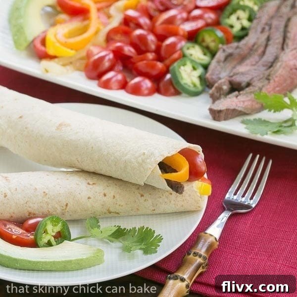 Two perfectly assembled Grilled Flank Steak Fajitas, brimming with tender steak, colorful vegetables, and fresh toppings, presented on a white dinner plate, ready to be enjoyed.