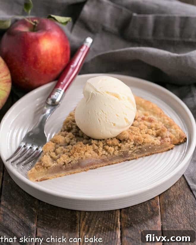Apple Pie Pizza slice with a scoop of ice cream on a white dessert plate, evoking warm fall feelings.