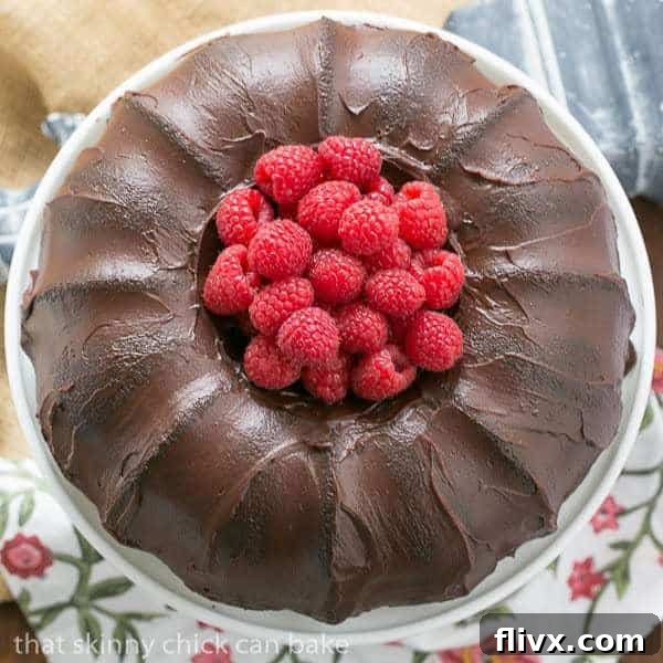 Rich Chocolate Buttermilk Bundt Cake on a white cake stand, garnished with fresh, vibrant raspberries, showcasing its beautiful fluted design.