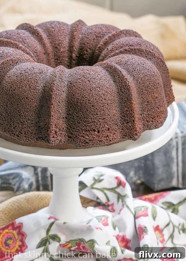 Delicious Chocolate Buttermilk Bundt Cake on a white ceramic cake stand, placed next to a elegant floral napkin, highlighting its moist texture.