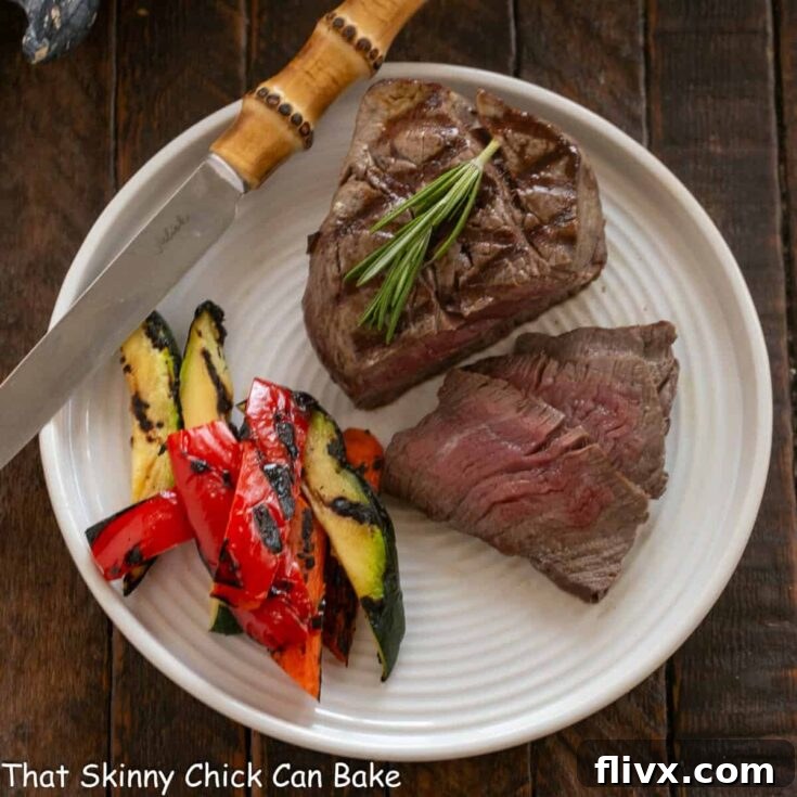 Overhead view of partially sliced filet mignon on a white plate with sauce.