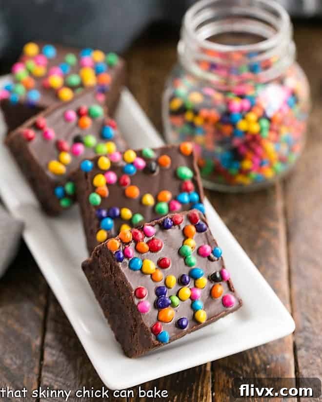 A tray of freshly baked homemade cosmic brownies with a small jar of colorful rainbow chip sprinkles.